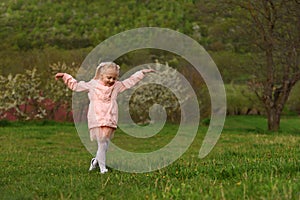 Little running girl in pink outfit walking in green meadow. Child walks through clearing in spring park