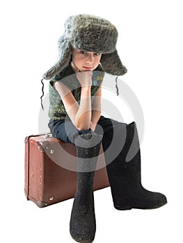 The little Russian boy in a fur hat and boots sitting on old suitcase and thinking