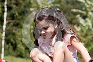 Little sad beautiful girl in a pink t-shirt with pigtails on the playground