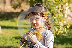 A little sad beautiful preschooler girl with yellow flowers in her hair stands outdoors on a blurred summer backgroundA little sad