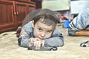 A little sad boy with a pensive look. Little boy playing toy cars at home on the carpet