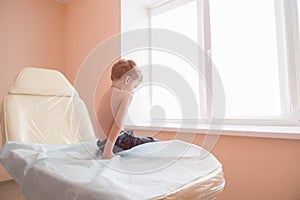 Little sad boy sit in hospital couch