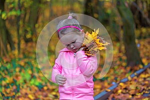 Little sad girl holding fallen leaves in autumn park. Young sorrowful child holds leaf. Small heartbroken female in dark forest.