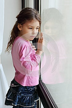 Little sad girl looks out window