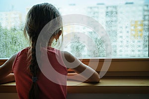 Little sad girl pensive looking through the window glass with a lot of raindrops. Sadness  and loneliness childhood concept image.