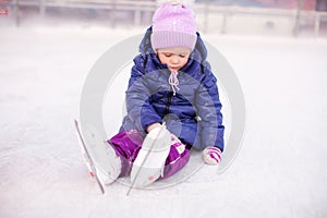 Little sad girl sitting on a skating rink after