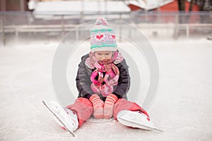 Little sad girl sitting on a skating rink after