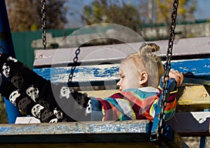 Little sad girl on a swing in the park.