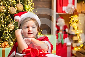 Little Santa Claus girl gifting gift. Funny kid holding Christmas gift. Cute little child near Christmas tree. Winter