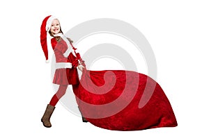 Little Santa Claus Girl Pulling Huge Red Christmas Bag Full of Gifts.  Funny Child in Santa Hat and Costume Carrying Big Sack with