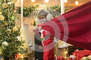 Little Santa Claus pulling huge bag of gifts on Christmas background. Santa helper carrying sack full of gifts. Funny