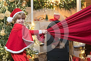 Little Santa Claus pulling huge bag of gifts on Christmas background. Santa child. Merry christmas and happy new year