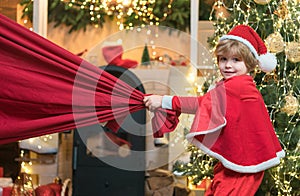 Little Santa Claus pulling huge bag of gifts on Christmas background. Santa child. Merry christmas and happy new year