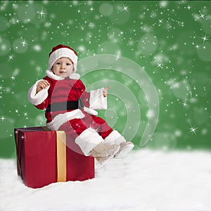 Little santa claus seated on a Christmas present in the snow