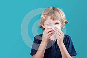 Little school boy with blonde hair sneezing to handkerchief and having runny nose. Flue, cold, allergy and disease concept