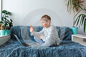 Little school boy having video call, online class on laptop during covid quarantine lockdown