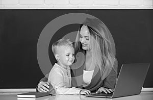 Little school child son using laptop with mother. Elementary school classroom. Teacher and schoolchild pupil in class