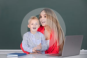 Little school child son using laptop with mother. Teacher tutor helping school child in class at school.