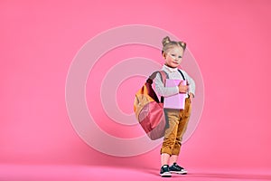 Little school girl with a notebook and backpack - isolated over a pink background