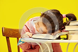 Little school girl sitting at table, tired, put her head on books, expresses fatigue from studying and difficulties in