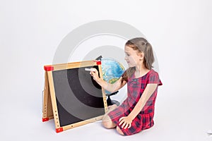 A little school girl of 7 years old sits in a red dress with a blackboard and writes with chalk on a white isolated background,