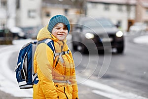 Little school kid boy of elementary class walking to school during snowfall. Happy child having fun and playing with