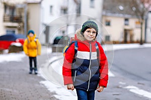Little school kid boy of elementary class walking to school during snowfall. Happy child and student with eye glasses