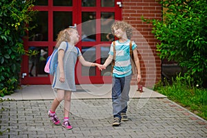 Little school students go on a schoolyard holding hands.