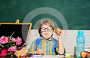 Little schoolboy in glasses eating apple at lunch time. Healthy breakfast. Delicious food for lunch. Primary school kid