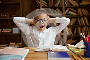 Little schoolboy screaming covering ears sitting at home table with homework