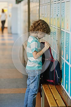 Little schoolboy standing near lockers in school hallway.