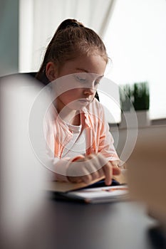 Little schoolchild holding literature book studying for online lesson