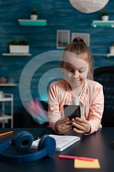 Little schoolchild holding modern smartphone reading literature story