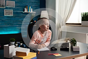 Little schoolchild sitting at desk table in living room doing mathematics homework