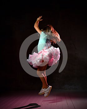 Little schoolgirl in blue t-shirt, poofy skirt and sneakers. She is bouncing up against black background, side view. Full length