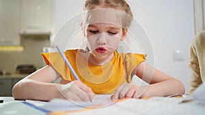 A little schoolgirl diligently does her homework. mom sits next to her