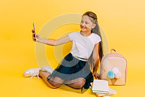 Little schoolgirl girl taking a selfie on a smartphone on a yellow background