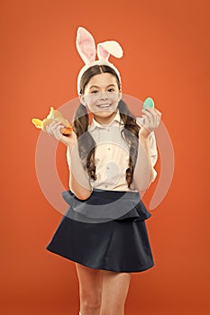 Little schoolgirl in rabbit ears hold carrot. Easter eggs. Happy easter. Origins of Easter Traditions. Small girl bunny photo