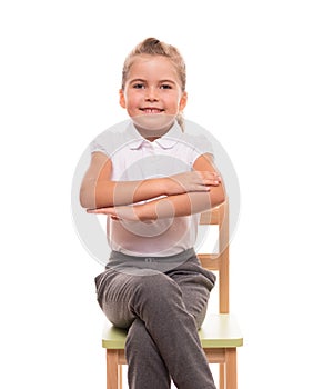 Little schoolgirl sitting on a chair and holding her hands in fr