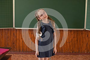 Little schoolgirl standing at the blackboard. Schoolgirl with two pigtails in glasses