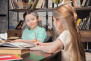 Little schoolgirls sitting at table and looking at each other