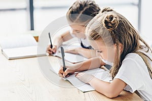little schoolgirls writing in notebooks while doing homework