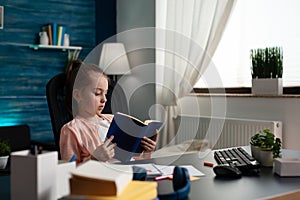 Little schoolkid holding school book studying for online literature lesson