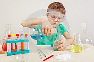 Little scientist in safety goggles doing chemical experiments in laboratory