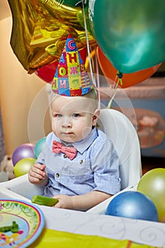 Little serious boy in birthday cap sits on