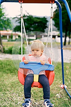 Little serious girl sitting on a swing