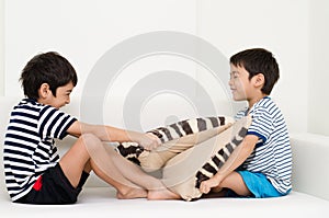 Little sibling boy playing pillow fighting on sofa