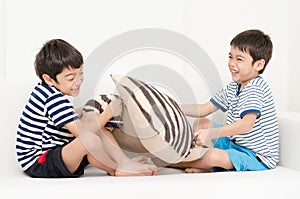 Little sibling boy playing pillow fighting on sofa