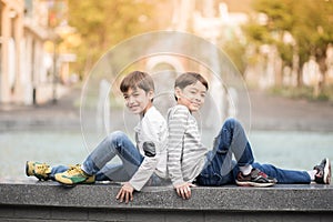 Little sibling boy sitting together at fountain outdoor