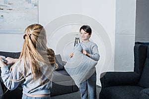 Little siblings in pajamas fighting with pillows at home